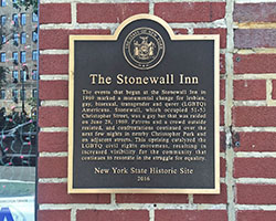 A brick wall with a plaque on it, which reads "The Stonewall Inn" and has a historical description underneath.