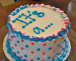 A circular white cake that reads "It's a..." with blue and pink dots