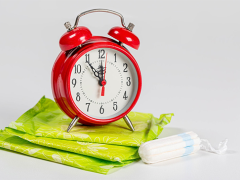 A red alarm clock sitting on top of a pile of green sanitary pads next to a tampon